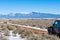 Four wheel drive vehicle on muddy dirt road curving towards snow-capped mountains