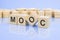 four wooden blocks with the letters MOOC on the bright surface of a pale lilac background. the inscription on the cubes