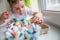 A four-year-old boy with a painted face lying on the windowsill puts Easter eggs in a craft box. Eggs in focus