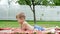 A four year old boy reads a book, in the garden, lying down on a blanket, a coverlet, on grass, lawn, in the summer