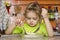 A four year old girl eats with a fork and spoon sitting at the table in the kitchen