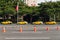 Four yellow taxis waiting for customers along the street that near the park with orange traffic cones, trees and building.
