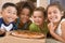 Four young children indoors with pizza smiling