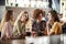 Four Young Female Friends Meeting Sit At Table In Coffee Shop And Talk