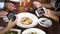 Four young people using mobile phone and taking photos of spaghetti and food at restaurant