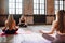 Four young women do complex of stretching yoga asanas in loft style class. Females meditate with closed eyes, back view