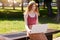 Foxy haired woman working with laptop in open air while sitting on bench in park, charging her device on innovative bench built in