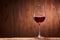 Fragile goblet of the red wine on the wooden stand on wooden wall background.