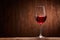 Fragile goblet of the red wine on the wooden stand on wooden wall background.