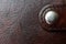 Fragment of a brown genuine leather product with a buttoned round metal button clasp. Back and background. Macro