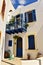 The fragment of characteristic white street of Greece with the blue balcony, windows and vases with flowers. Mandraki. Greece.