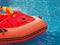Fragment of a children's red inflatable boat floating in a blue outdoor pool