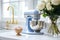 Fragment of classic white kitchen. Blue planetary mixer with stainless steel bowl, cup with ingredients, bouquet of