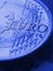 Fragment of a coin of 1 one euro. In focus inscription with the name of the Eurozone currency. Close-up. Blue tinted vertical