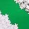 Fragment of a folded white jigsaw puzzle and a pile of uncombed puzzle elements against the background of a green surface. Texture