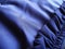 A fragment of a garment made of synthetic polyester fabric. The play of light and shadow on blue material. Right - sewn decorative