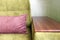 Fragment of a green sofa with a wooden armrest and a pink pillow