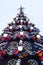 A fragment of a huge Christmas tree with many ornaments, gift boxes and luminous lamps. Photo of a decorated Christmas tree close-