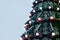 A fragment of a huge Christmas tree with many ornaments, gift boxes and luminous lamps. Photo of a decorated Christmas tree close-