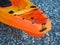 Fragment of an orange single sea kayak on a pebble sea shore