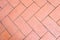 Fragment of a park sidewalk of herringbone pattern, paved with reddish stone plates.