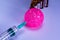 Fragment of a syringe stabbing a pink ball and blurred ampoules. Vaccination, antivirus concept. Close-up. Selective focus