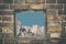 Fragment of the wall of an old house with a bricklaying of red brick and and view from small window with cloud sky