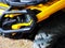 Fragment of a yellow quad bike with headlights black bumper and rough dirty wheel