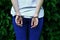 Fragment of a young criminal girl`s body with hands in handcuffs against a green blossoming ivy leaves