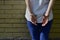 Fragment of a young criminal girl`s body with hands in handcuffs against a yellow brick wall background