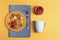 Fragrant mini pancakes in an orange plate stand on a blue napkin, next to them is a blue ceramic mug and there is a jar of jam