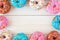 Frame of assorted donuts with pastel icing against white wood