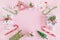 Frame from colorful Christmas decorations, caramel sticks and gift boxes with artificial snow on a pink background.