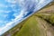 The frame is divided diagonally between a green meadow, a field, a forest with trees and a gray sky with clouds and thunderclouds