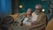 In the frame an elderly couple are sitting on a sofa under a plaid. They are attentively watching a movie or program on