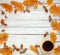 A frame made of autumn leaves and acorns with a cup of coffee on a white wooden background. Flat layout.