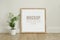 Frame, poster mock up with wooden frame. Empty frame standing on the wooden floor with a green plant. Free space for
