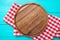 Frame of round cutting board and red plaid tablecloth. Blue wooden background in the cafe. Top view. Macro