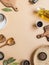 Frame of small bowls various dry spices, wood kitchen utensils, olive oil in glass bottle on beige background. Top view. copy