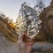 Frame Square Man holding a translucent and glistening chunk of ice against a mountain