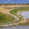 Frame Square Paved pathway curving along the rocky and grassy lake shore under cloudy sky