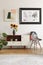 Framed photo and abstract art above sunflowers on an elegant cabinet and a patchwork chair in white living room interior.