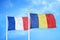 France and Romania two flags on flagpoles and blue cloudy sky