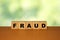 FRAUD message word on a wooden desk on cube blocks with a green nature