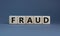 Fraud symbol. Concept word `fraud` on wooden cubes on a beautiful grey table. Grey background. Business and fraud concept