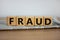 Fraud symbol. Wooden cubes placed on a newspaper. The word `fraud`. Beautiful wooden table. White background. Business and fraud