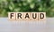 FRAUD word written on wooden blocks. The text is written in black letters and is reflected in the mirror surface of the table