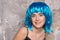 Freak concept. Lady on smiling face posing in blue wig, concrete wall background. Woman with blue hair looks unordinary