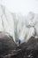 A free climber with an ice ax in his hand stands at the foot of the Great Glacier next to an epic crack in the fog in