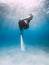 Freediver glides over sandy sea with white fins. Attractive woman free diver in blue ocean